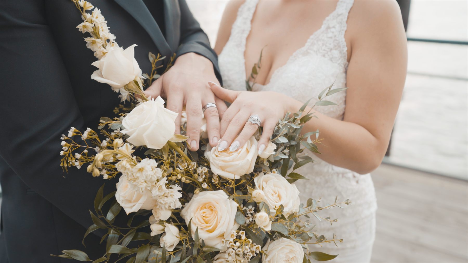 Wedding rings held over a white rose bouquet